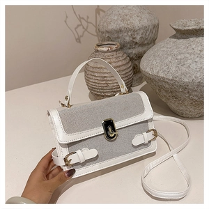 Detail of white textured crossbody bag featuring gold buckle and leather strap