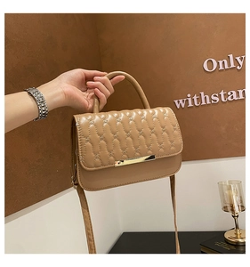 Detalle de bolso bandolera beige acolchado con diseño ondulado y broche de metal dorado