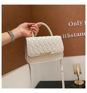Detalle de bolso bandolera de cuero beige grabado con hebilla dorada y acolchado fino