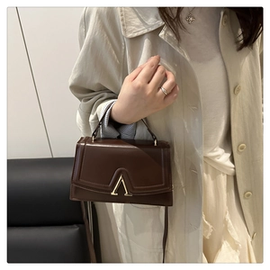 Detail view of dark brown leather handbag with elegant gold V-shaped metal buckle clasp