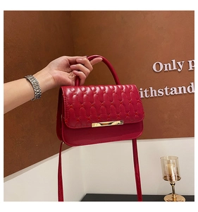 Detalle de bolso de cuero rojo acolchado con hebilla de metal dorado y asa superior