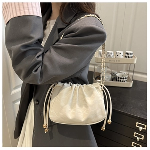 Detail of white pleated cloud bag with drawstring closure and gold metal ball accents
