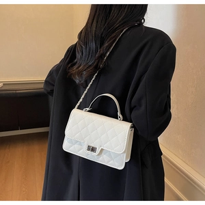 Detail view of white quilted crossbody bag with metal chain strap and twist lock clasp