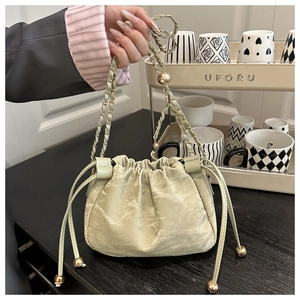 Detail of light green ruched bucket bag with gold chain strap and metal drawstring beads
