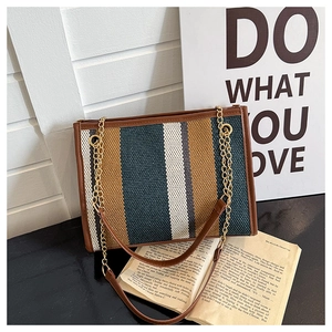 Detail of striped tote bag with brown leather trim and golden chain strap on a black surface