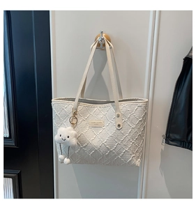 Close-up of white quilted tote bag with branding plate and plush cloud charm accessory