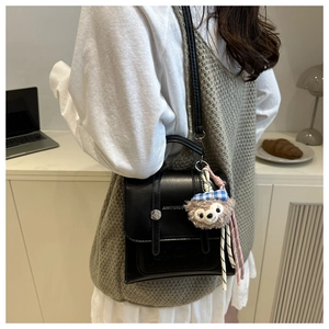 Close-up of retro black faux leather handbag with belt buckles and teddy bear charm