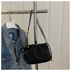 Dettaglio borsa a secchiello nera plissettata con tracolla a sfere dorate su denim