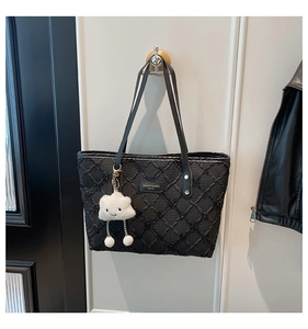 Detail of black quilted tote bag featuring a brand name plate and a cute plush charm