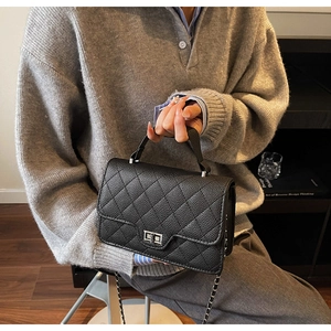 Detail of black quilted leather texture and silver metal lock on a classic crossbody bag