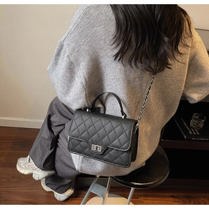 Detail of black quilted leather shoulder bag with silver turn-lock and chain strap