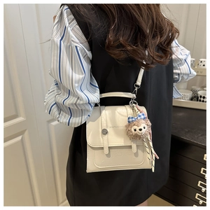 Detail of white PU leather flap bag with letter print and plush doll charm on the shoulder strap