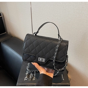 Detail of black quilted leather texture and silver metal twist lock on classic chain bag