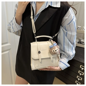 Detail of cream vintage faux leather handbag featuring AIWITUXCOOLS print and plush bear