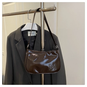 Close-up of glossy brown leather underarm bag with embossed heart and letter M logo