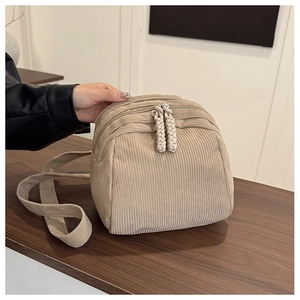 Detail of beige corduroy shell bag showing soft ribbed texture and dual braided zip pullers