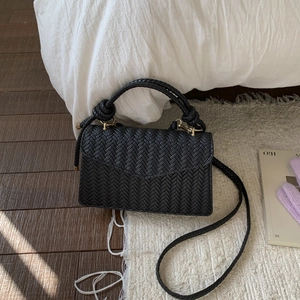 Minimalist black woven flap handbag with thick handle and golden hardware on soft white rug