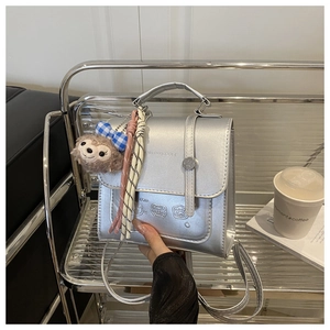 Detail of silver metallic mini backpack with bear charm on chrome display stand