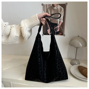 Close-up of black leopard print velvet tote bag held by a model in a cozy home setting