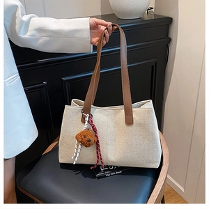 Detail of canvas tote bag with brown leather handles and a plush bear pendant charm
