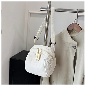 Dettaglio della trama in velluto a coste bianco crema e doppia zip di una borsa a tracolla
