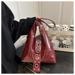 Detail of burgundy glossy leather tote featuring wide strap with silver rivets and metal eyelets