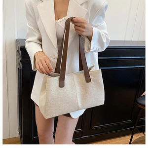 Close-up detail of beige canvas tote bag with dark brown leather straps on model