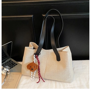 Detail of canvas tote bag with black leather straps and cute brown plush puppy charm