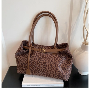 Detail of leopard print tote bag with brown straps and gold buckle on white props