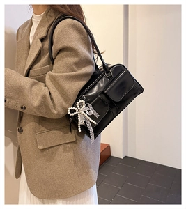 Detail of black leather shoulder bag with pearl lace bow charm and pocket accents
