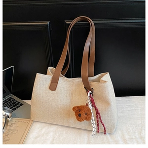 Close-up of beige woven tote bag featuring brown leather straps and a cute bear charm
