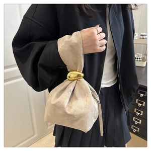 Detail of beige suede bucket bag with unique gold pebble ring handle on a black coat