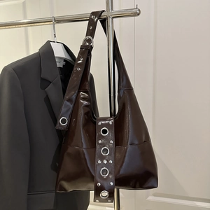 Dark brown patent leather shoulder bag with silver studs and metal eyelets on a stand