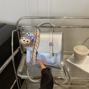 Silver metallic vintage handbag with cartoon embossing and plush charm on a display stand