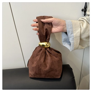 Detail of dark brown suede bucket bag featuring a unique pebble-shaped gold metal buckle