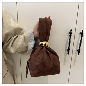 Detail of a brown suede bucket bag featuring a unique gold bean-shaped metal clasp
