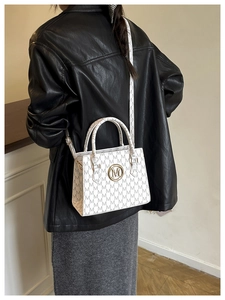 Model trägt eine weiße Monogramm-Tragetasche mit goldenem M-Logo und Schultergurt
