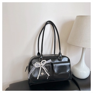 Détail du sac à bandoulière noir brillant avec double poches et charm nœud en perles et dentelle