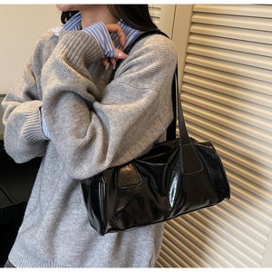 Close-up of black glossy patent leather baguette bag styled with a grey sweater