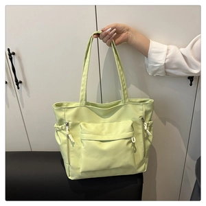 Close-up of light green tote bag showing side zipper pockets and front flap pocket