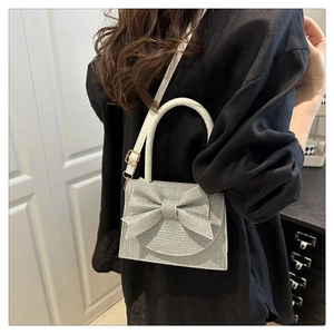 Detail view of silver glitter bag featuring large bow decoration and white handle