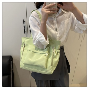 Detail view of light green nylon tote bag featuring front flap and drawstring pockets