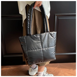 Detail of black quilted tote bag with padded handles and shiny puffer fabric texture