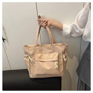 Detail of a large beige tote bag with functional drawstring side pockets and zip pocket