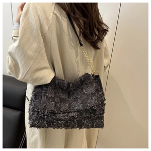 Detail of dark grey tweed crossbody bag with gold chain strap on beige coat