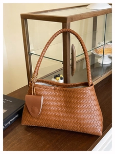 Gros plan sur la texture en cuir tressé marron et le pendentif de ce sac cabas