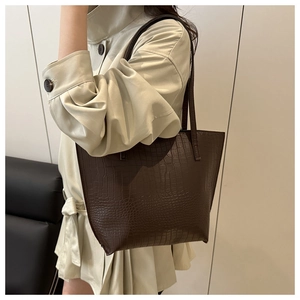 Detail of dark brown crocodile-textured tote bag worn by a model in a trench coat