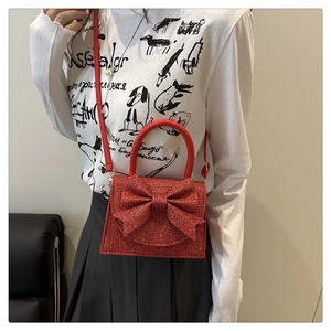 Detail of red glitter evening bag with bow showing strap and handle worn by model