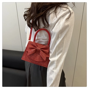 Detail of red glitter evening bag featuring a large bow and elegant round handle