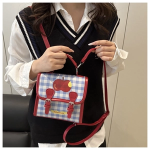 Detail of red and blue plaid crossbody bag with apple patch and red leather handle